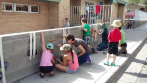 campers, interns, and staff work on a mural on a brick wall by the library in the summer of 2017.