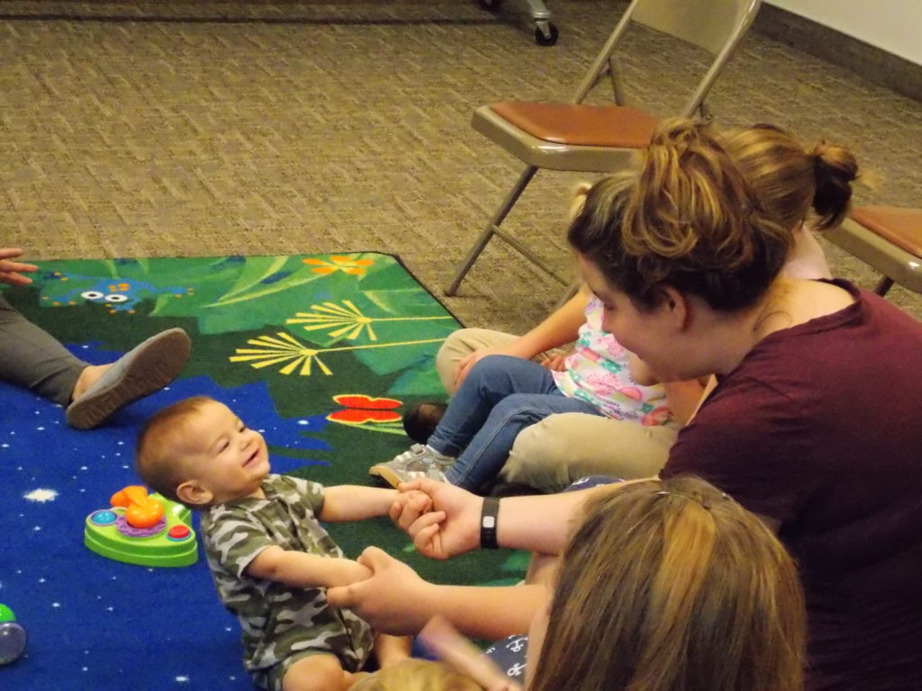 A mother holds a baby's hands while he leans backwards, smiling, at the first Babytime program on October 5, 2016