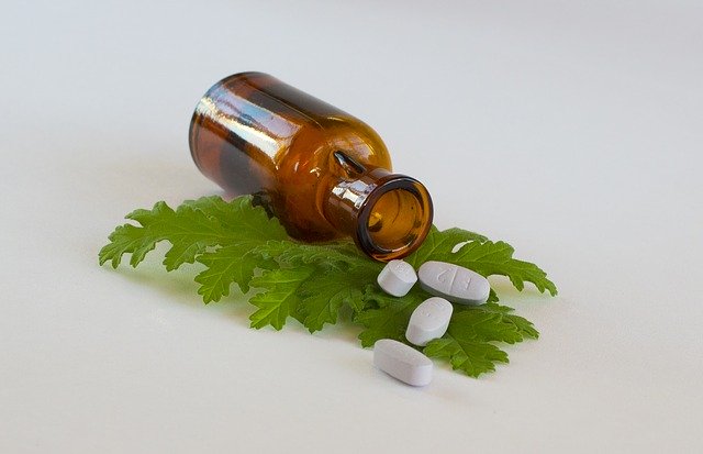 brown glass bottle and several white pills on a green leaf