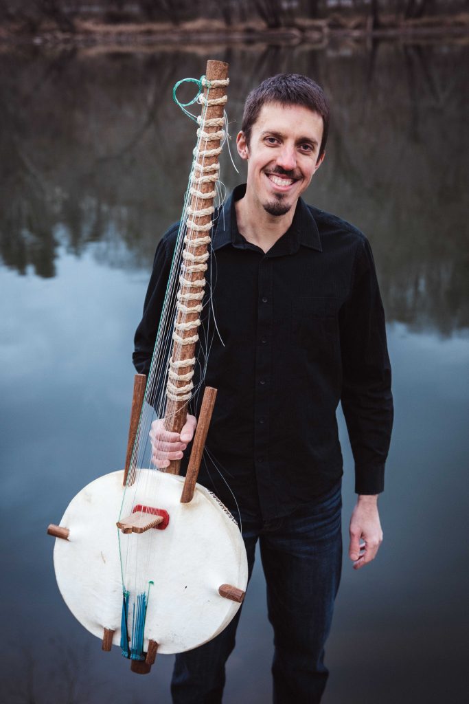 photo of Sean Gaskell holding his kora in front of a body of water